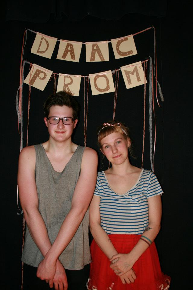 Two young people standing in front of a handmade DAAC PROM banner