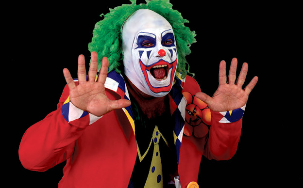 Photo of a scary clown with green wig and red jacket.