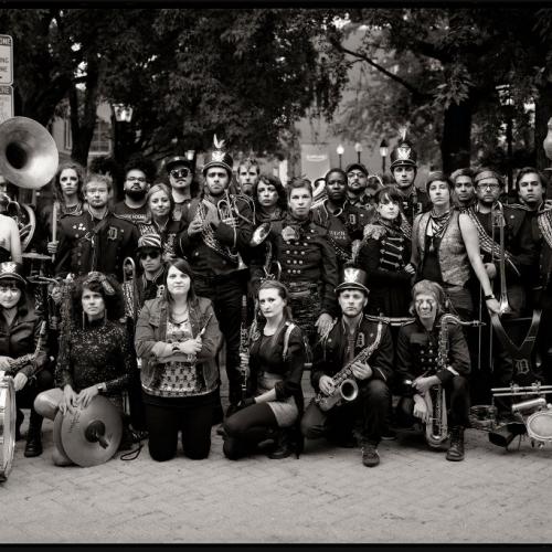 Large group of musicians in eclectic marching band costumes posing in the street