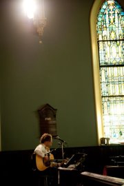 Guitarist stands at a mic near a stained glass window