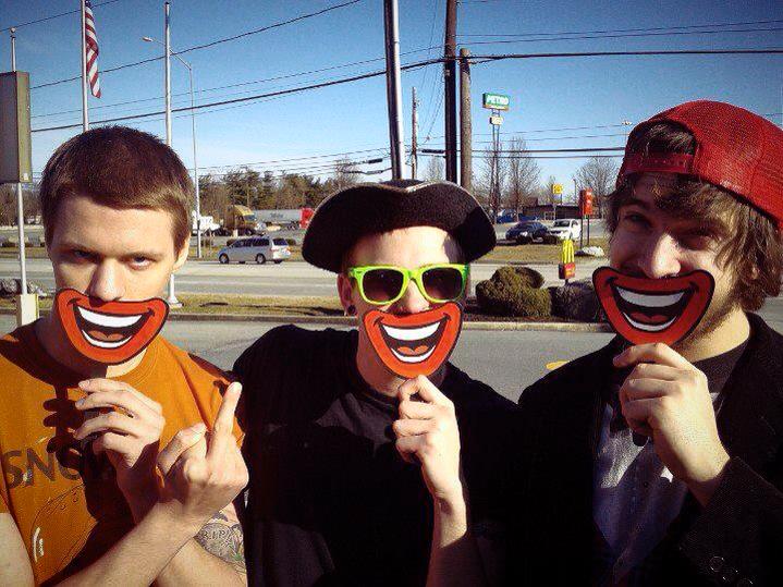 Three men standing on the street holding smiley face signs in front of their mouths