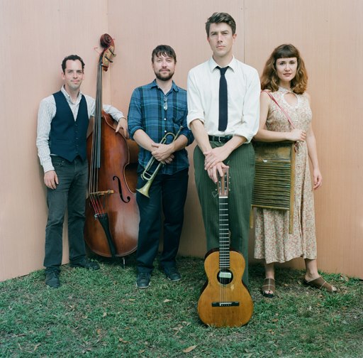 Photo of band members holding instruments and standing on grassy lawn