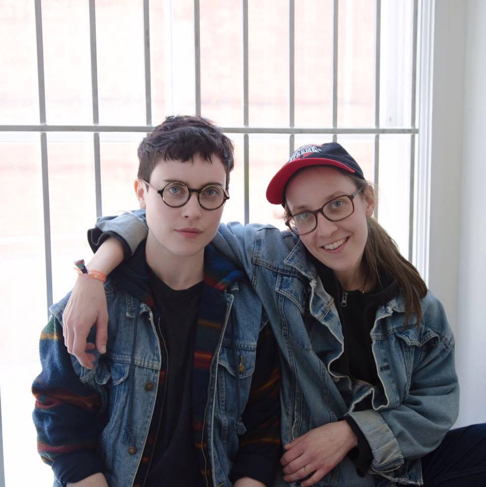 Two young, content people smiling and relaxed in front of a window.