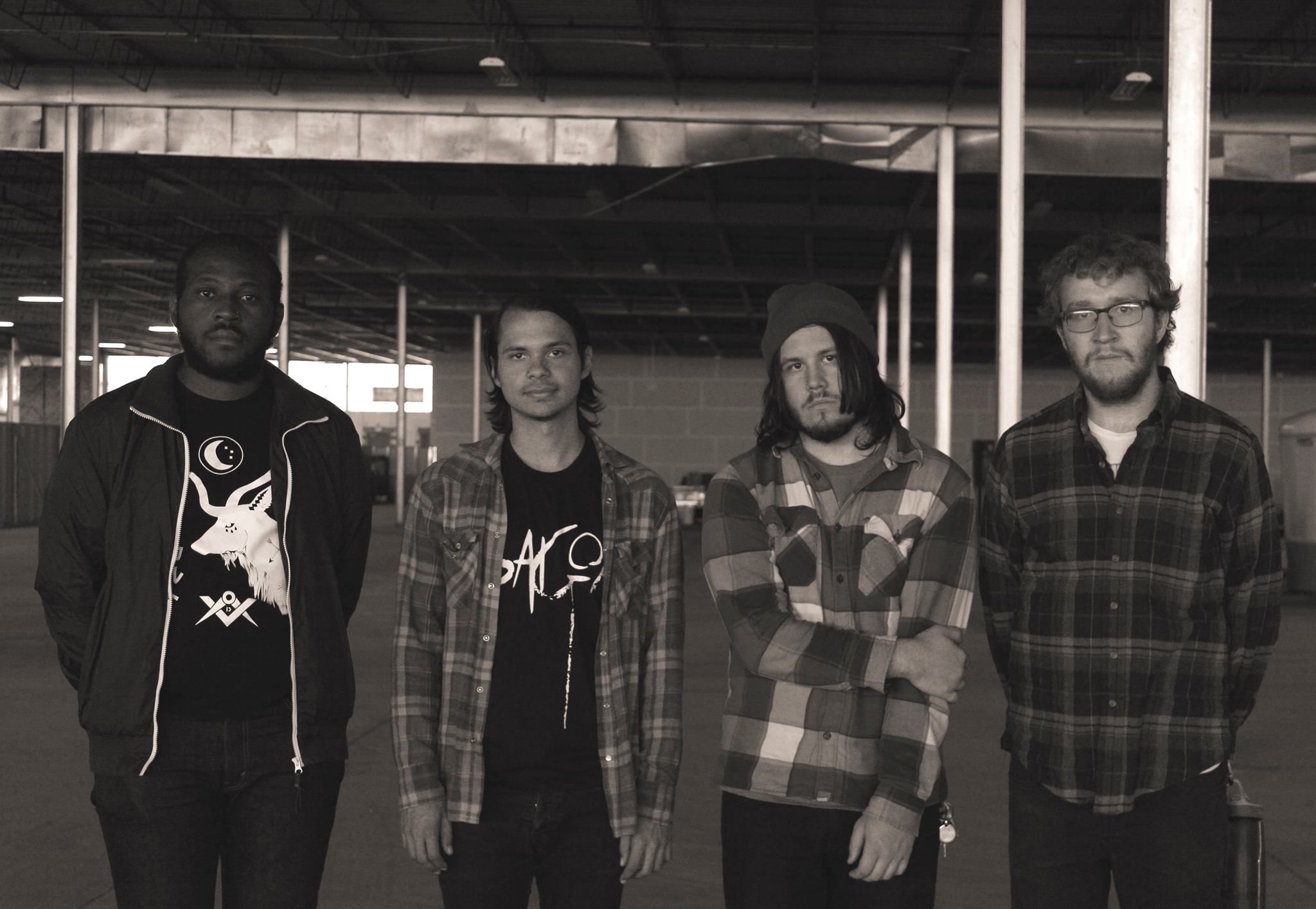 Black and white photo of the four members of House Olympics, standing in an empty industrial building