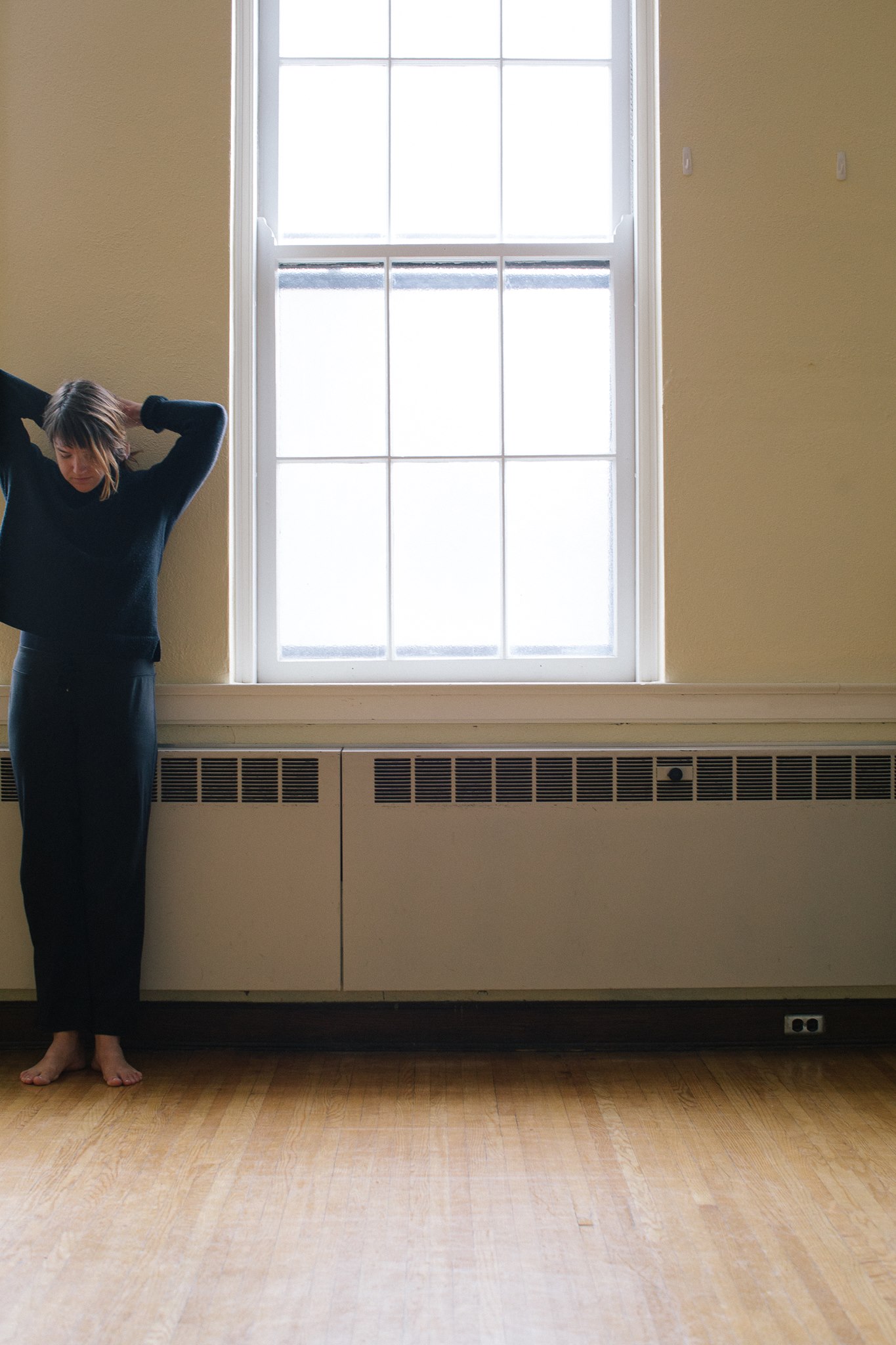 A person with straight, sandy brown hair stands next to a beige wall and window