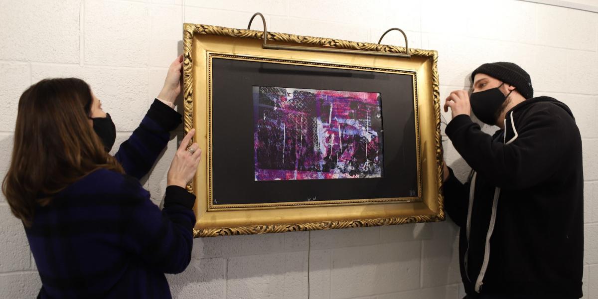 Masked volunteers hang a framed painting in the DAAC gallery