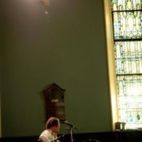 Guitarist stands at a mic near a stained glass window