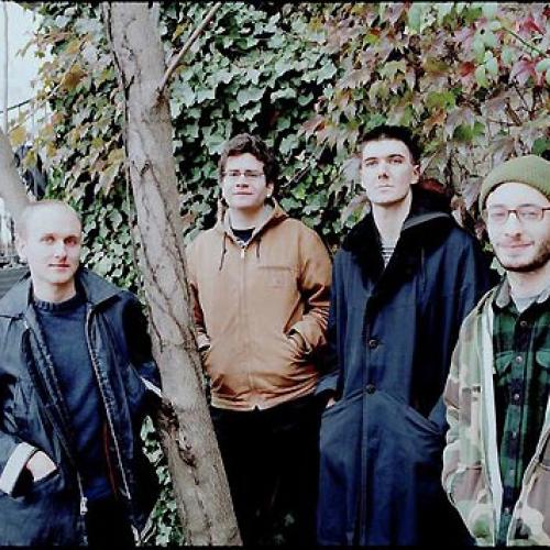 Four men in jackets stand next to a tree.