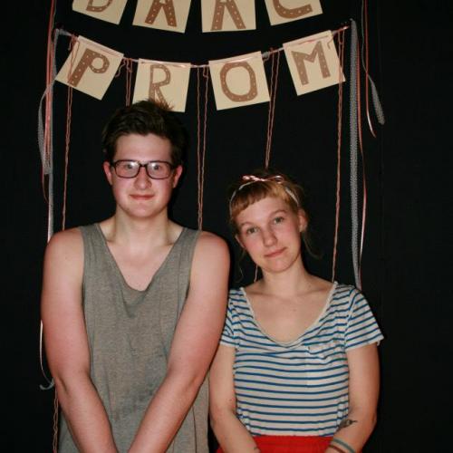 Two young people standing in front of a handmade DAAC PROM banner