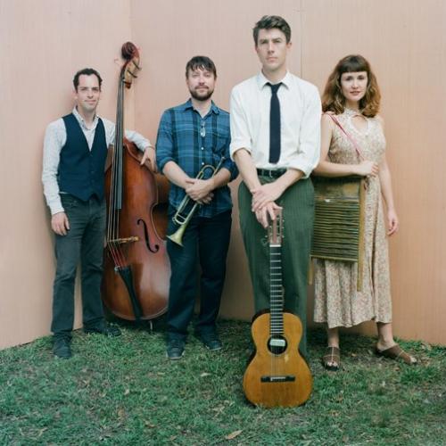 Photo of band members holding instruments and standing on grassy lawn