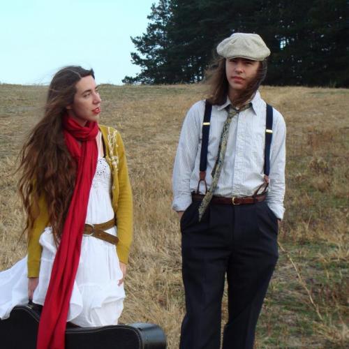 A man and woman standing in a field, she is holding a guitar case.