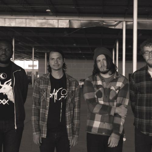 Black and white photo of the four members of House Olympics, standing in an empty industrial building